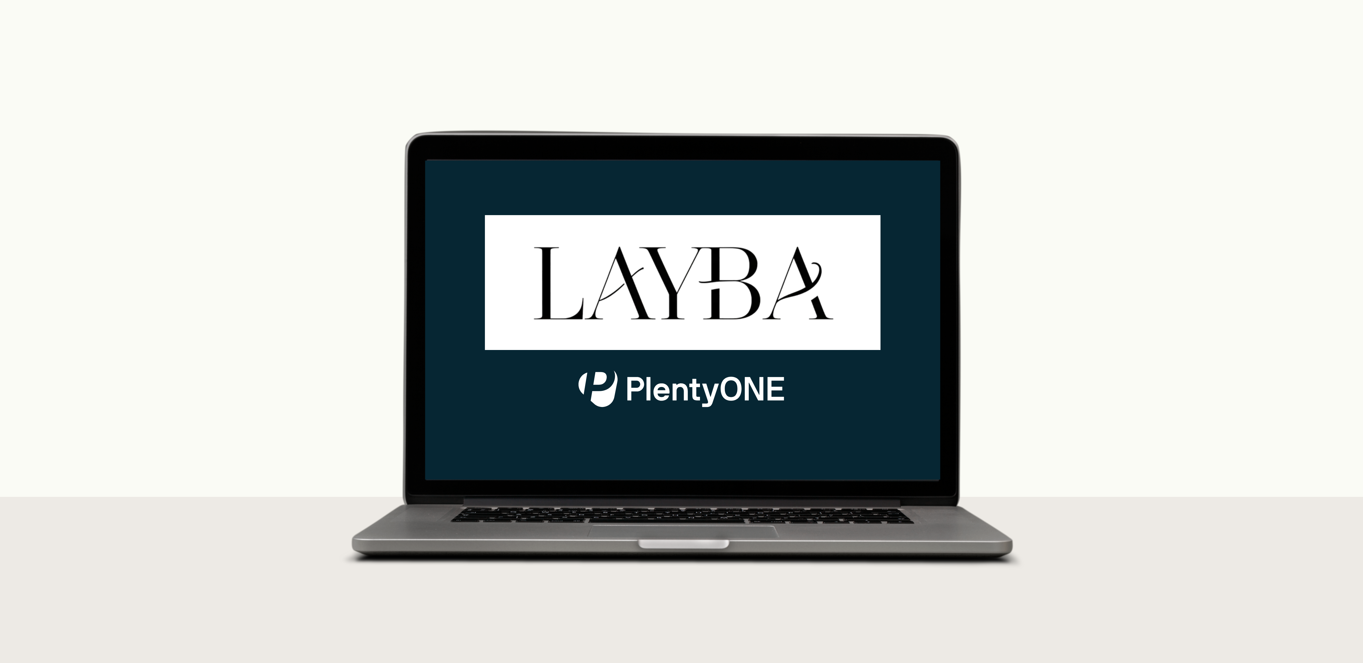 Ein MacBook-Laptop, dessen Bildschirm eingeschaltet ist und einen dunkelblauen Hintergrund anzeigt. Ein weißes Rechteck in der Mitte zeigt das Logo von „LAYBA“ in einer eleganten Serifenschrift. Darunter befindet sich das Logo von PlentyONE. Der Laptop steht auf einer hellgrauen Oberfläche vor einem schlichten weißen Hintergrund.
