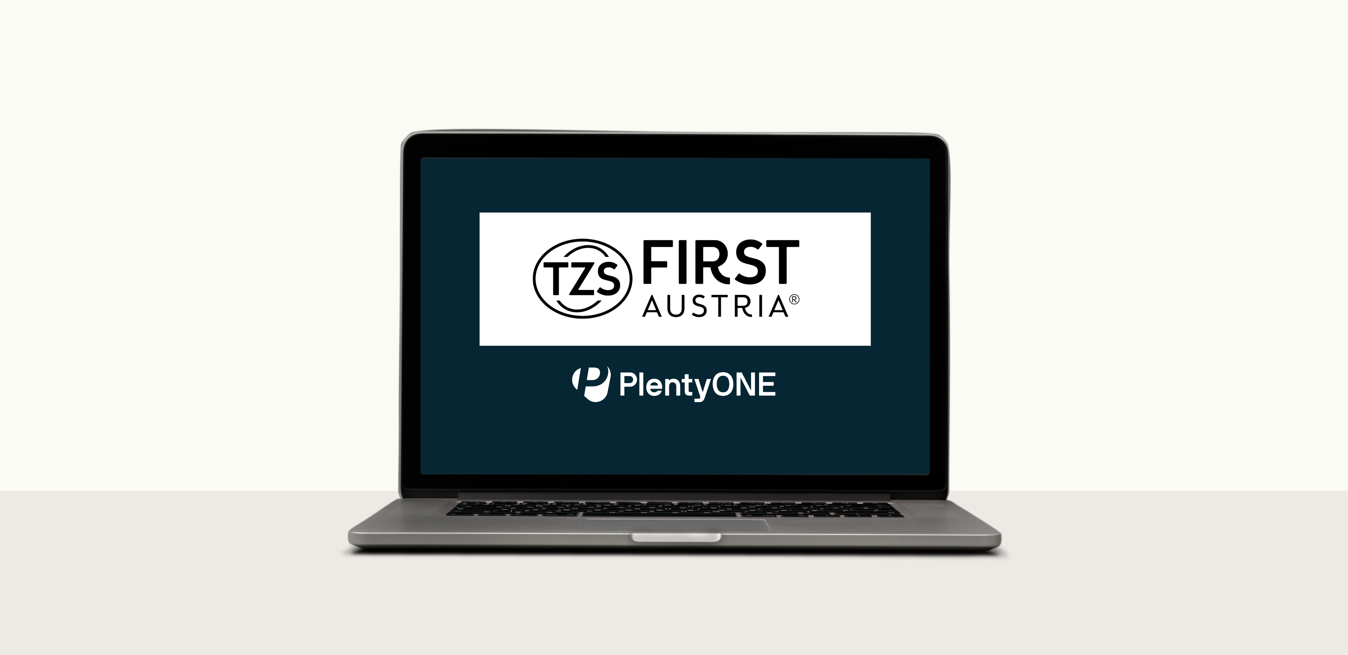 Ein MacBook-Laptop, dessen Bildschirm eingeschaltet ist und einen dunkelblauen Hintergrund anzeigt. Die Logos von zwei Unternehmen sind sichtbar: "TZS First Austria" in einem weißen rechteckigen Kasten und "PlentyONE" darunter. Der Laptop steht in der Mitte des Bildes auf einer hellgrauen Oberfläche, vor einem schlichten weißen Hintergrund.
